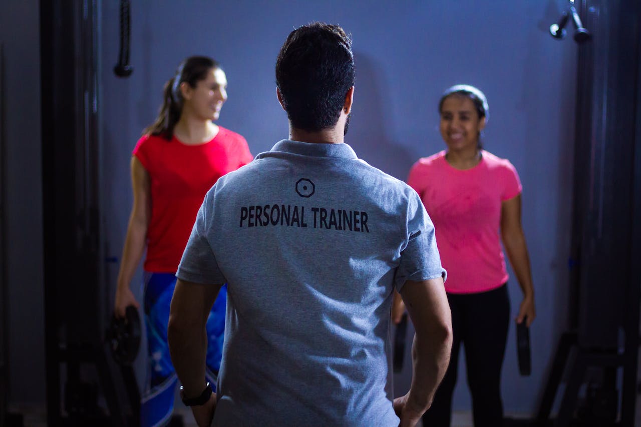 services-03 Back view of a personal trainer guiding two women during a gym session indoors.