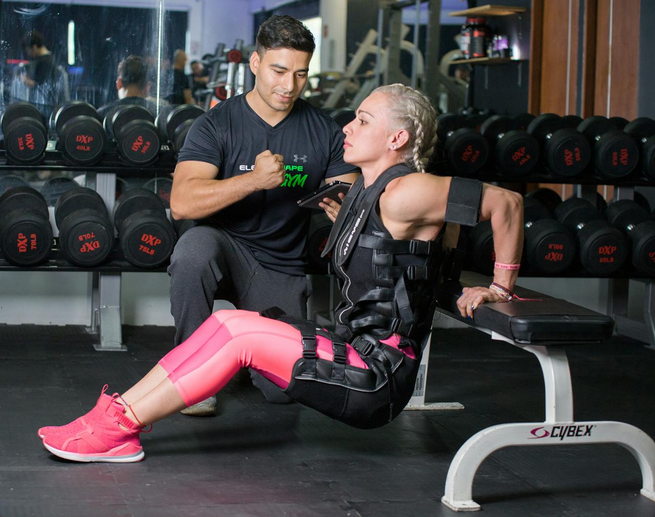 services-02 Woman doing tricep dips with personal trainer support in a gym setting.